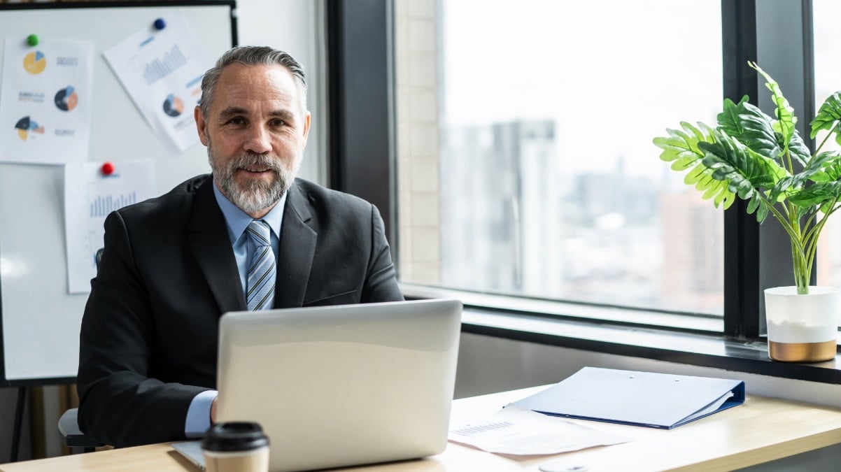 A man in a suit sits at a desk with a laptop, discussing hospital readiness for managing episode risk with the CMS team.